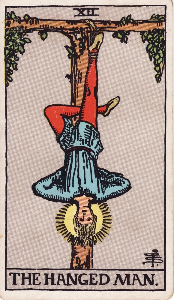 A calm young man hanging upside down by one foot from a living tree, a soft halo around his head
